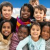 A group of diverse kids smile in this portrait. They are stacked on top of each other while cuddling in close and showing how happy they are.