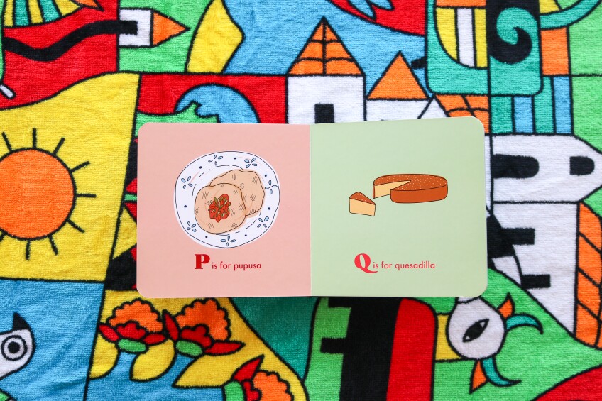 open book with illustration of a pupusa on one page and a cheesecake like bread on the other