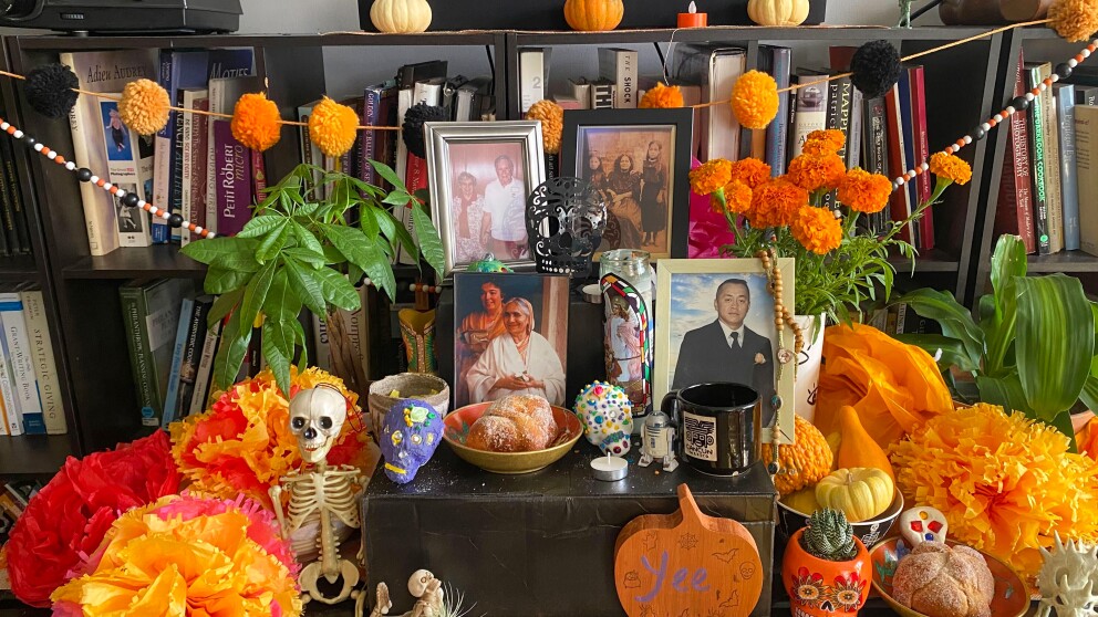 a dia de los muertos altar on a table decorated with orange marigolds made of paper, photos, pan de muerto and skulls