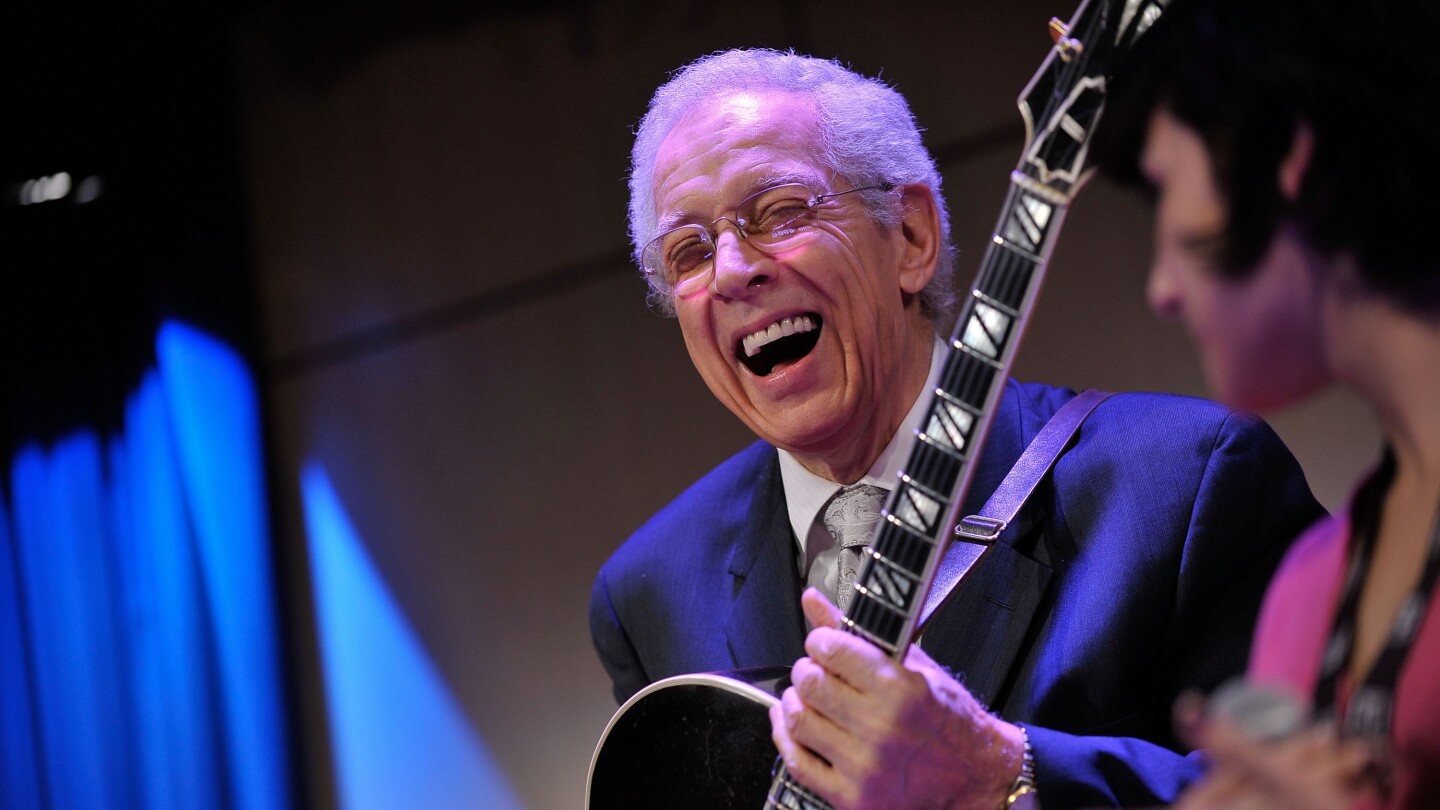 Kenny Burrell is an older man holding a guitar smiling wholeheartedly