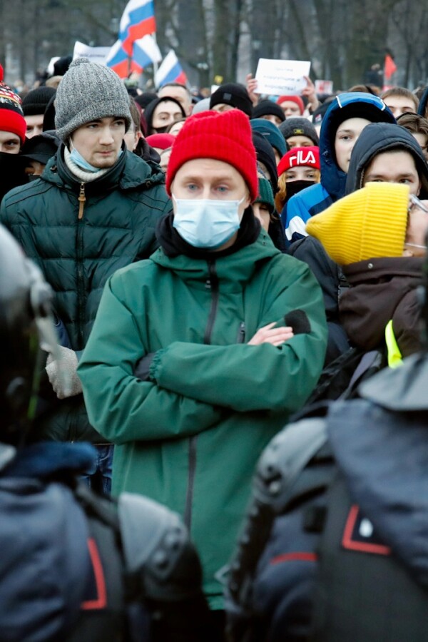 A person stands defiantly with their arms crossed in front of police.