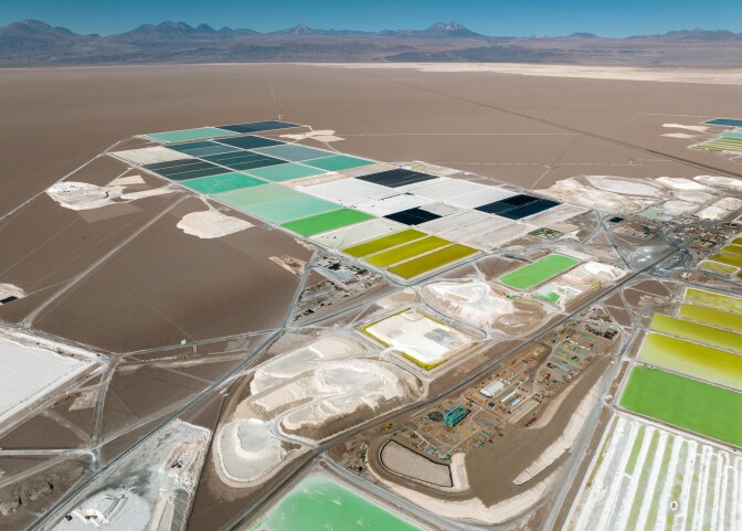 A grid of rectangular pools with multi-colored brine stands out against a barren desert landscape and a blue sky aboe