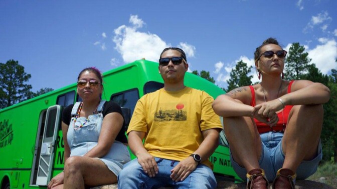 Three people wearing sunglasses sit with a bright green van behind them.