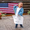 A small child holds their fist in the air and holds a sign that reads "I'm gonna change the world." 